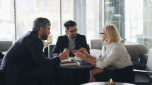 Tre affärspersoner diskuterar vid ett bord med dokument och pennor