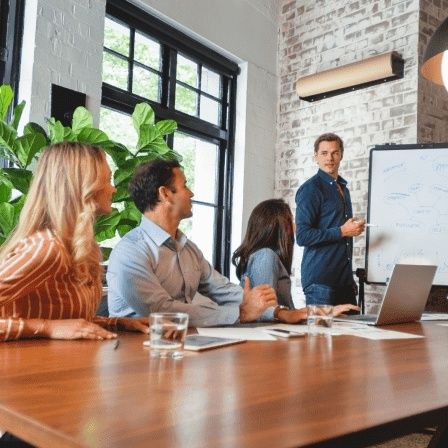 Möte där en person presenterar vid whiteboard för en arbetsgrupp